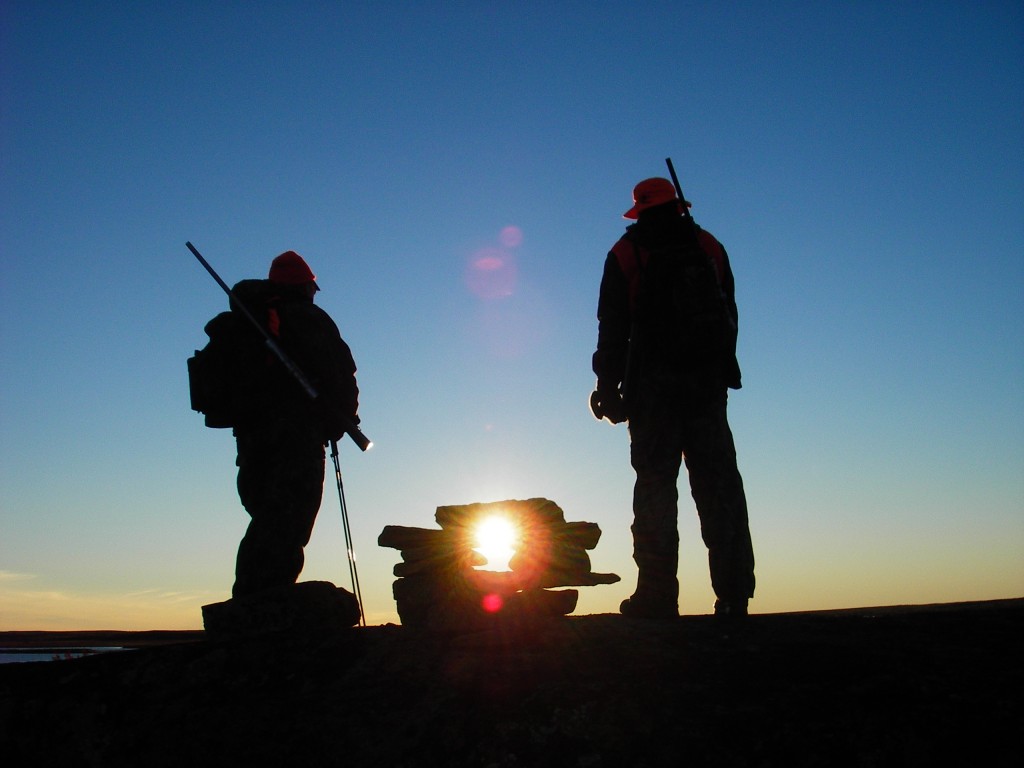Hunters inspect an inukshuk build on the rocks.